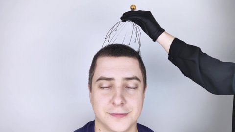 A man is given a head massage with a capillary massager in the salon. The client's face shows relaxation and joy. The concept of anti-stress massage and the provision of services by a masseur.