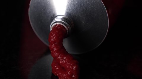 Pressing out red tomato puree of a aluminium tube, macro view
