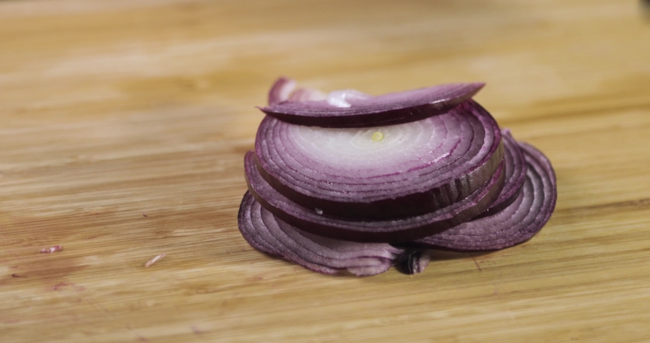 Slicing red onion in kitchen using knife. Cook in gloves is preparing vegeterian healthy food, salad. Chef in gloves cooking chopping fresh red onion on wooden board, hands closeup.