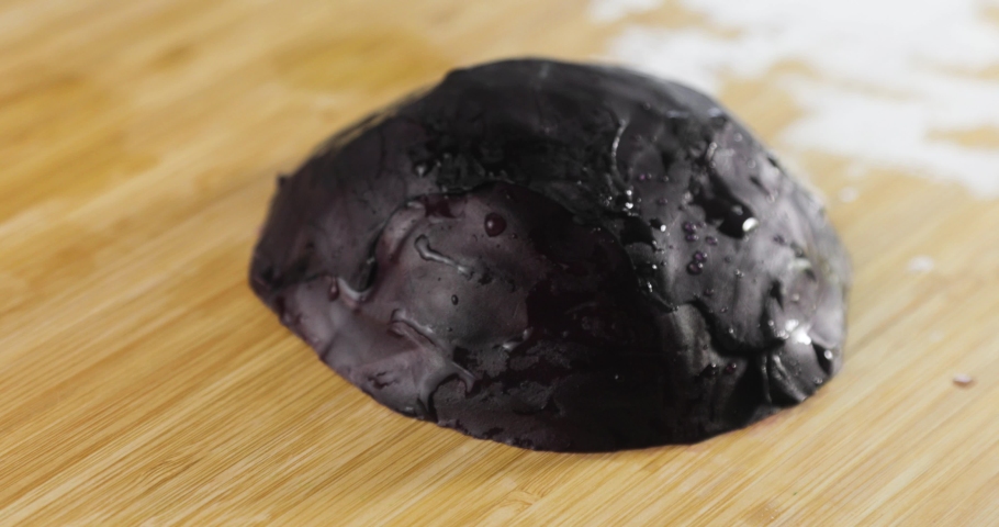 Cook is preparing vegeterian healthy food, salad. Chef is cooking cutting fresh red cabbage on wooden board, hands closeup. Slicing red cabbage in kitchen using knife.