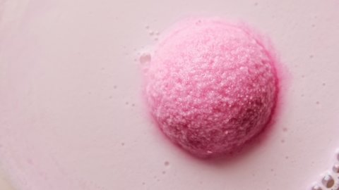 Pink bath bomb ball dissolves in water with white foam bubbles. Cosmetic product for relaxation in the bathroom, bath salt.