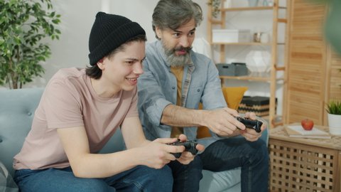 Portrait of father and son enjoying video game having fun doing high-five hand gesture indoors in apartment. Modern devices and family activities concept.