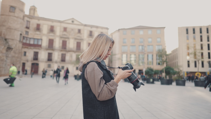 Beautiful Female tourist with dslr photo camera walking through old town square, Barcelona, Spain. She takes photos