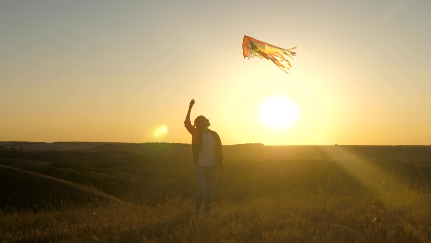 A happy girl runs with a kite in her hands across field in rays of the sunset. A healthy child dreams of freedom, flight. Kid plays outdoors in the park. Teen wants to be a pilot | Shutterstock HD Video #1066335235