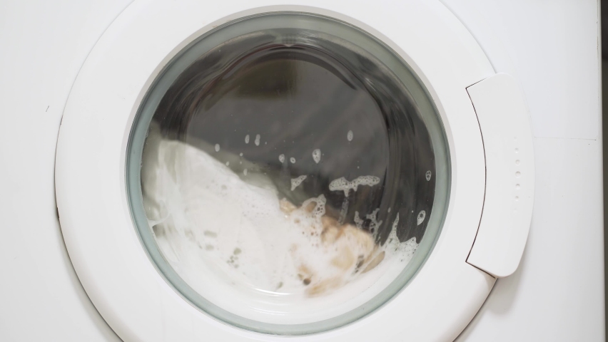 Washing clothing in domestic washing machine in home. Close-up video of spinning drum washing machine.
