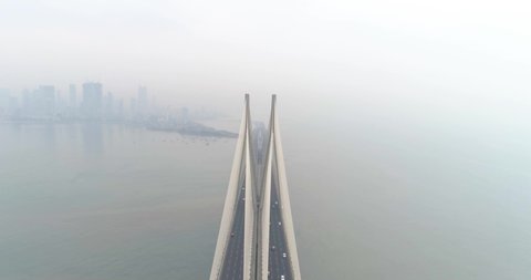 A drone shot at Bandra Worli Sea Link seen from an aerial view in slow motion. Cinematic drone movement with the iconic Mumbai Sea Link at the forefront and the city view in the background.