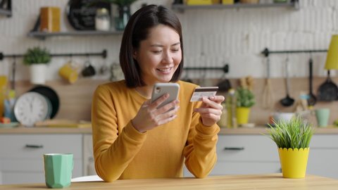 Multi ethnic female client holding banking credit card and smart phone using instant mobile payments. Happy mixed race asian customer shopper making purchase on smart phone e-banking service concept