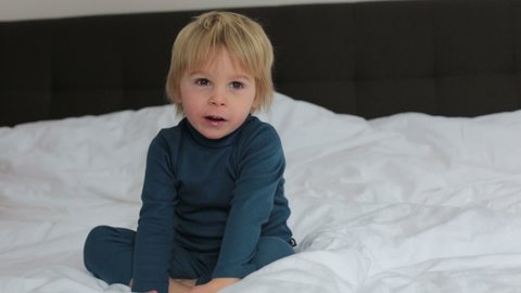 Cute blond toddler child, sucking his foot thumb, making funny faces, laughing