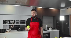Man chef juggling apples with one hand and dropping them cooking in modern kitchen. Funny guy food blogger juggling fruits shooting video for cuisine blog.