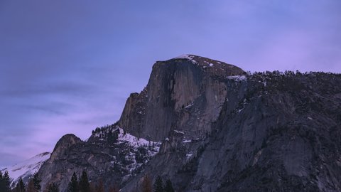 Time lapse sunset with steep rock in Yosemite Valley National park USA. Clouds over scenic Half Dome mountain. Pink sunlight shining over massive summit peak. World famous landmark nature landscape.