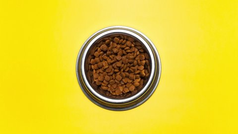 Stop motion animation photography. Top view of dry food for cats disappear from round steel bowl on yellow background.