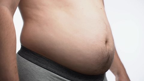 Close-up, male stomach, overweight. Young man with a naked fat belly shakes fat folds on his stomach, obesity, health, beer belly