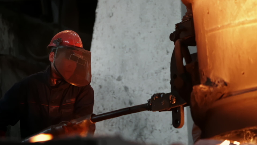 Factory Man in a Protective Mask Works in a Foundry holds the industrial oven. Heavy Work of the Metallurgy. Furnace Fire. Heavy Metallurgist industry. Metallurgist Workshop. Metal Cast, Slow Motion | Shutterstock HD Video #1066357885