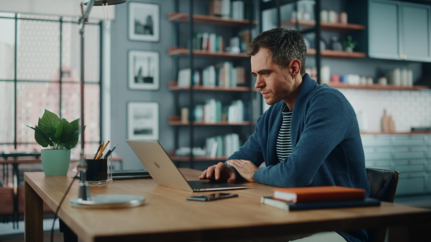 Handsome Caucasian Man Working on Laptop Computer while Sitting Behind Desk in Cozy Living Room. Freelancer Working From Home. Browsing Internet, Using Social Networks, Having Fun in Flat. Royalty-Free Stock Footage #1066358662