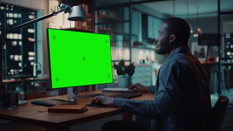 Handsome Black African American Specialist Working on Desktop Computer with Green Screen Mock Up Display at Home Living Room. Freelance Man Chatting to Clients Over the Internet on Social Networks.