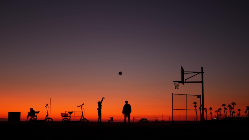 California summertime dusk beach aesthetic, pink sunset. Unrecognizable silhouettes, people play game with ball on basketball court. Newport ocean resort near Los Angeles CA USA. Purple sky gradient.