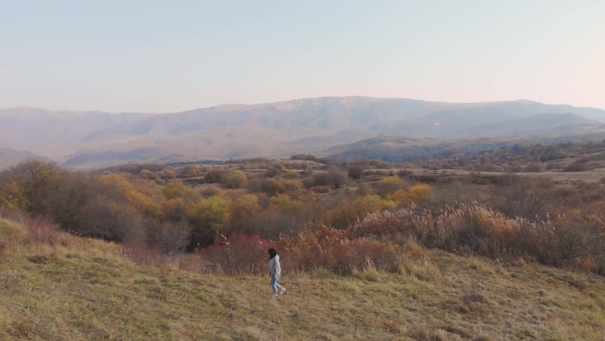 Female person walks in meadow field surrounded by autumn nature landscape. Relaxing and walks in nature concept