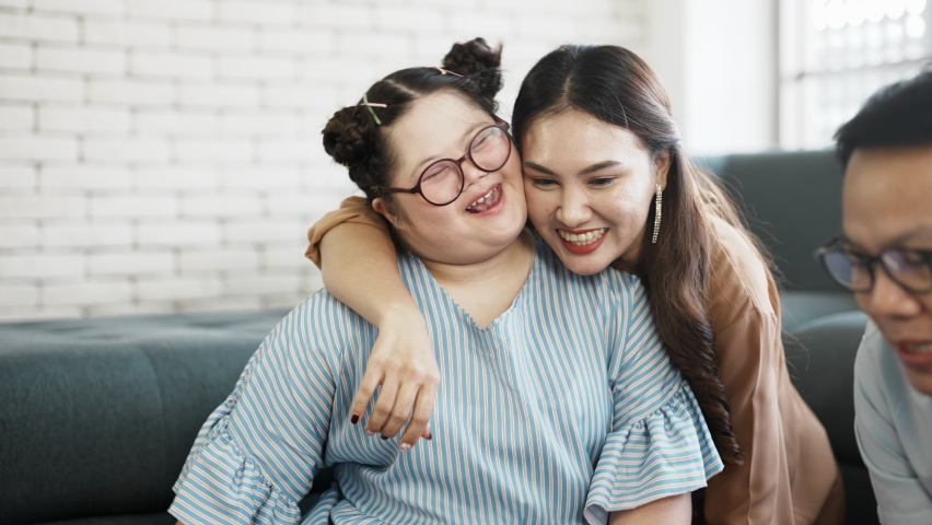 Down syndrome chubby girl doing activities together with parents in the living room at home, hugging sweet down syndrome daughter smiling with her mom. | Shutterstock HD Video #1066367407