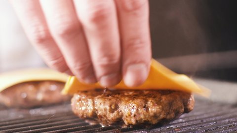 Man Put Chees On Meat Burger Cutlet On Hot Grill Pan. Cooking Food In Professional Restaurant Kitchen. Person Preparing Meal Dinner. Making Tasty Hamburger Dish. Delicious Home Modern Cuisine Close up