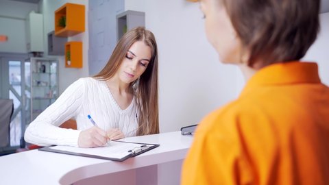young woman fills out a questionnaire at the reception. Patient being attended by a nurse in a medical consultation. Portrait of female patient and receptionist in dentist dental clinic or hospital