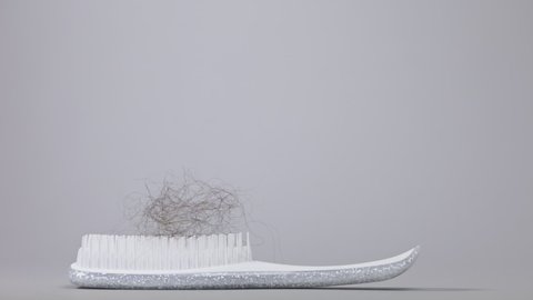 A torn tuft of hair falls on top of the white hair brush. Side view. Gray background. The concept of hair loss