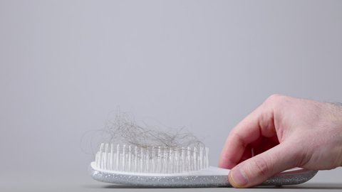 Alopecia. A male's hand puts down a hair brush with a bunch of fallen hair. Side view. Gray background. The concept of hair loss