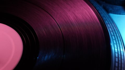 Close-up of a vinyl spinning on a dj turntable and illuminated by the lights of the club. Concept: disco, dancing, 90's, music