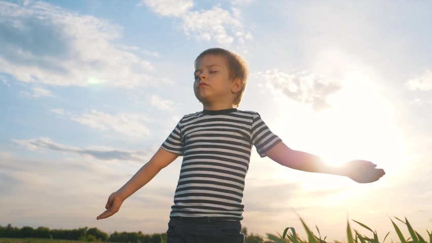 Happy kid praying in the park. Kid in a field with wheat praying raised his hands to the sides. Happy child closing his eyes looks to the sky. Child prays to the sky childhood dreams. Spiritual prayer