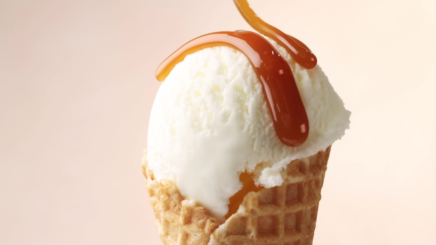 Melted caramel sauce flowing on rotating vanilla ice cream in waffle scoop close up | Shutterstock HD Video #1066388362