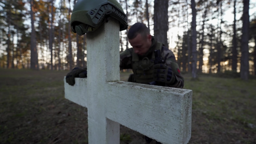Soldier in the woods paying respect to his fallen hero by the cross grave stone in day - wide angle full length military cemetery war and death concept