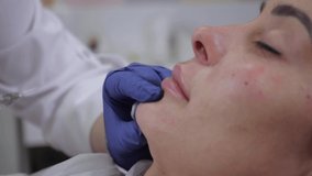 A beautician wearing medical gloves makes a cosmetic procedure to augment the chin. Video for a beauty salon. High quality 4k footage