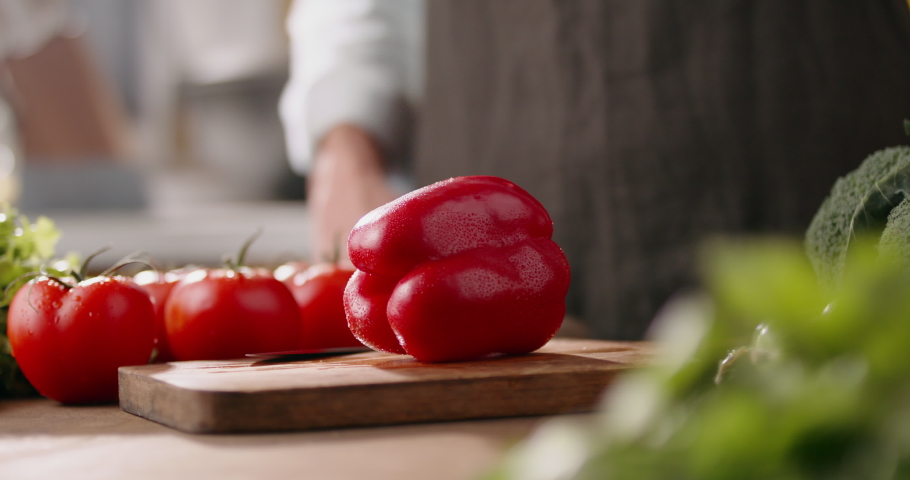 Close up shot of chef's hands cutting a fresh 
red bell pepper with knife on wooden board. Cooker preparing vegetarian salad in kitchen, 4k footage Royalty-Free Stock Footage #1066412356