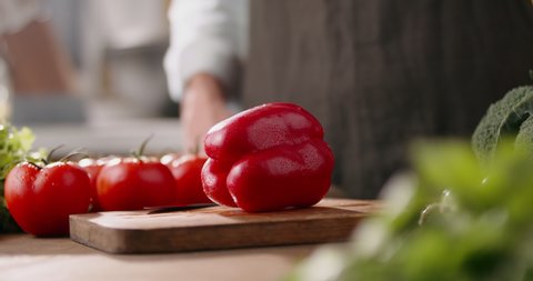Close up shot of chef's hands cutting a fresh 
red bell pepper with knife on wooden board. Cooker preparing vegetarian salad in kitchen, 4k footage