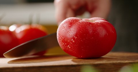 Close up shot of chef's hands cutting a fresh tomato with knife on wooden board. Cooker preparing vegetarian salad in kitchen, 4k footage