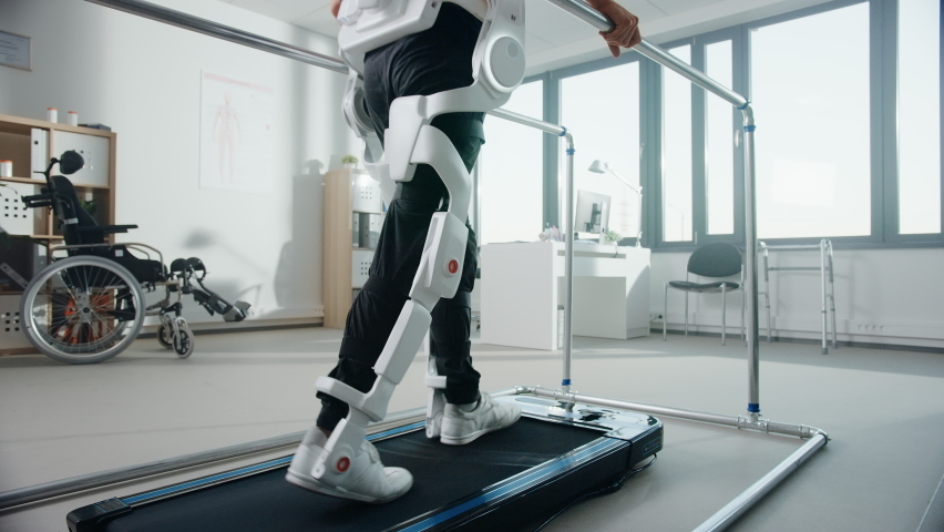 Modern Hospital Physical Therapy: Patient with Injury Walks Wearing Advanced Robotic Exoskeleton Legs. Physiotherapy Rehabilitation Technology to Make Disabled Person Walk Again. Focus on Legs Royalty-Free Stock Footage #1066412725