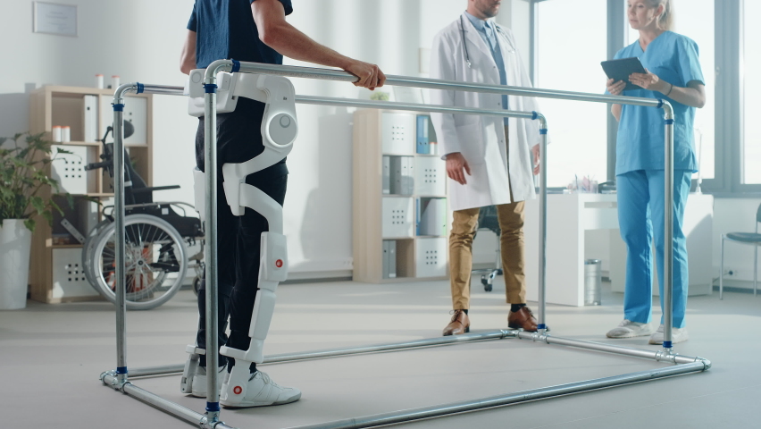 Modern Hospital Physical Therapy: Patient with Injury Walks Wearing Advanced Robotic Exoskeleton. Physiotherapy Rehabilitation Scientists, Engineers use Tablet Computer to Help Disabled Person | Shutterstock HD Video #1066412746