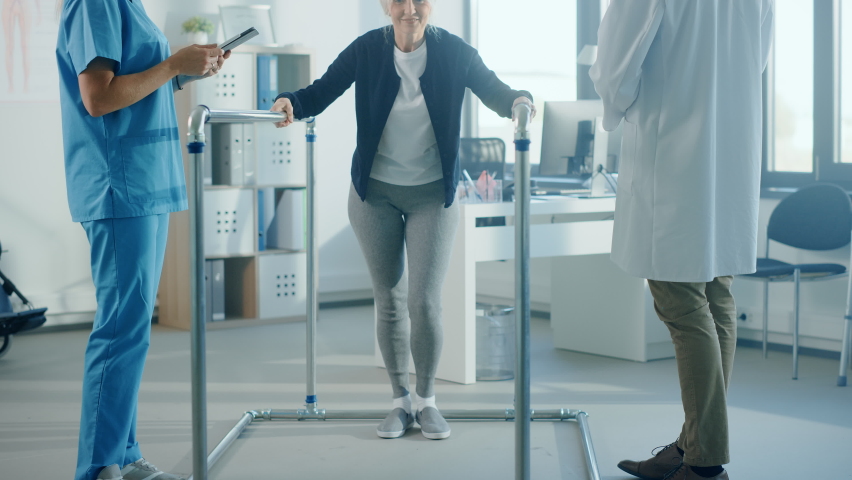 Hospital Physical Therapy: Portrait of Strong Senior Female Patient with Injury Successfully Walks Holding Parallel Bars. Physiotherapist, Rehabilitation Doctor, Help, Assist Disabled Patient | Shutterstock HD Video #1066412803