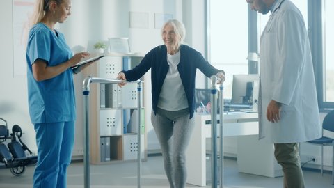 Hospital Physical Therapy: Portrait of Strong Senior Female Patient with Injury Successfully Walks Holding Parallel Bars. Physiotherapist, Rehabilitation Doctor, Help, Assist Disabled Patient