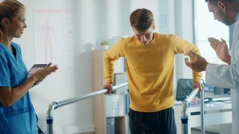 Hospital Physical Therapy: Portrait of Strong Male Patient with Injury Successfully Walks Holding Parallel Bars. Physiotherapist, Rehabilitation Doctor, Help, Assist, Disabled Person. Slow Motion