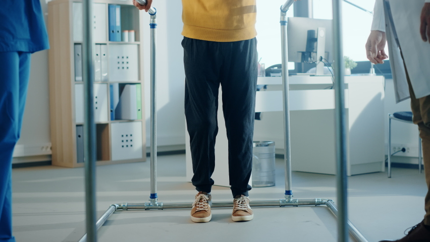 Hospital Physical Therapy: Portrait of Male Patient with Injury Successfully Walks Holding Parallel Bars. Physiotherapist, Rehabilitation Doctor, Help, Assist, Disabled Person. Elevating Slow Motion | Shutterstock HD Video #1066412821