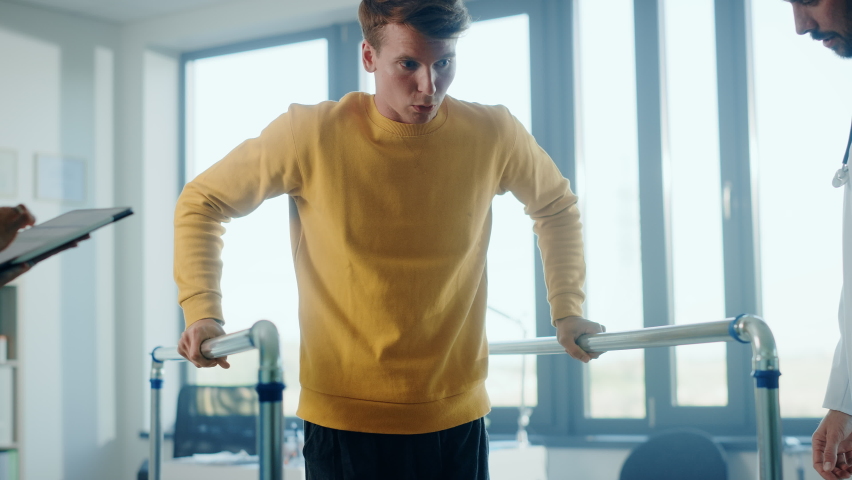 Hospital Physical Therapy: Portrait of Male Patient with Injury Successfully Walks Holding Parallel Bars. Physiotherapist, Rehabilitation Doctor, Help, Assist, Disabled Person. Elevating Slow Motion | Shutterstock HD Video #1066412821