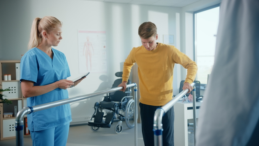 Hospital Physical Therapy: Strong Determined Male Patient with Injury Successfully Walks Holding Parallel Bars. Physiotherapist, Rehabilitation Doctor, Help, Assist, Encourage Disabled Person to Heal Royalty-Free Stock Footage #1066412833