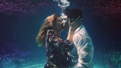 Cinematic tender art shot of young carefree romantic loving couple is kissing with passion in blu underwater with colorful water splash. Concept of love, relationship, freedom, sensuality, fantasy.