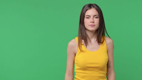 Cheerful brunette young woman 20s in yellow tank top isolated on green background studio. People lifestyle concept. Dancing doing dab hip hop dance hands move gesture youth sign hiding covering face
