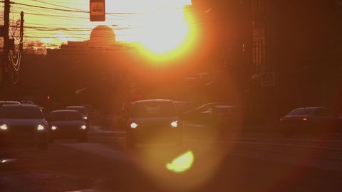 City street at sunset. Sow motion 2x. The sun sets between the houses. Cars are passing along the city road. 