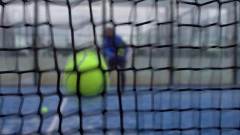 Slowmotion through grid view of paddle tennis man playing on blue court outdoors. One caucasian paddle player sportsman hitting the ball. Racquet sport game Concept.-Dan