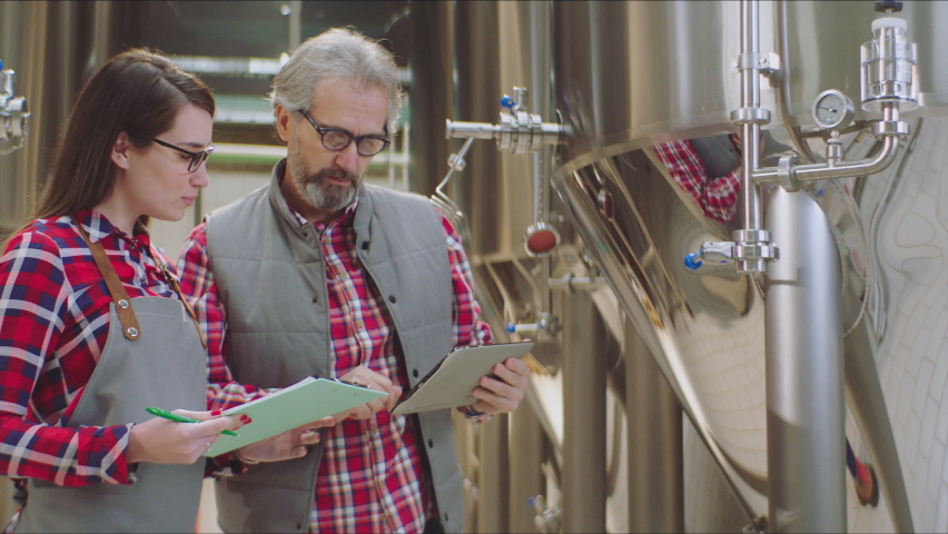 Two chemists in a brewery. Big brewery vats. Chemists taking notes in a factory. Factory, brewery concept. Royalty-Free Stock Footage #1066427134