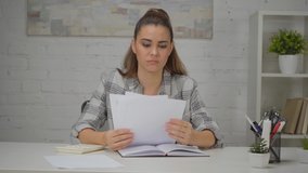 upset woman holding papers and praying while sitting at workplace