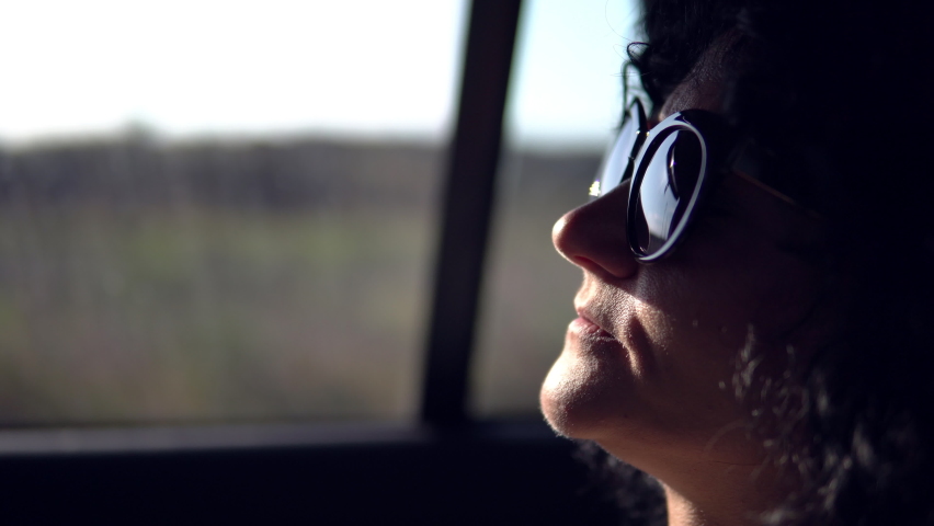 Trendy woman with curly hair and glasess traveling by car at backseat