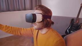 Virtual reality. Young man with VR set in his appartment, Guitar in the background. High quality 4k footage